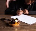 Judge signing documents at desk with focus on gavel, representing law and justice.