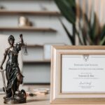 A framed Harvard Law School certificate beside a Lady Justice statue on an office desk.